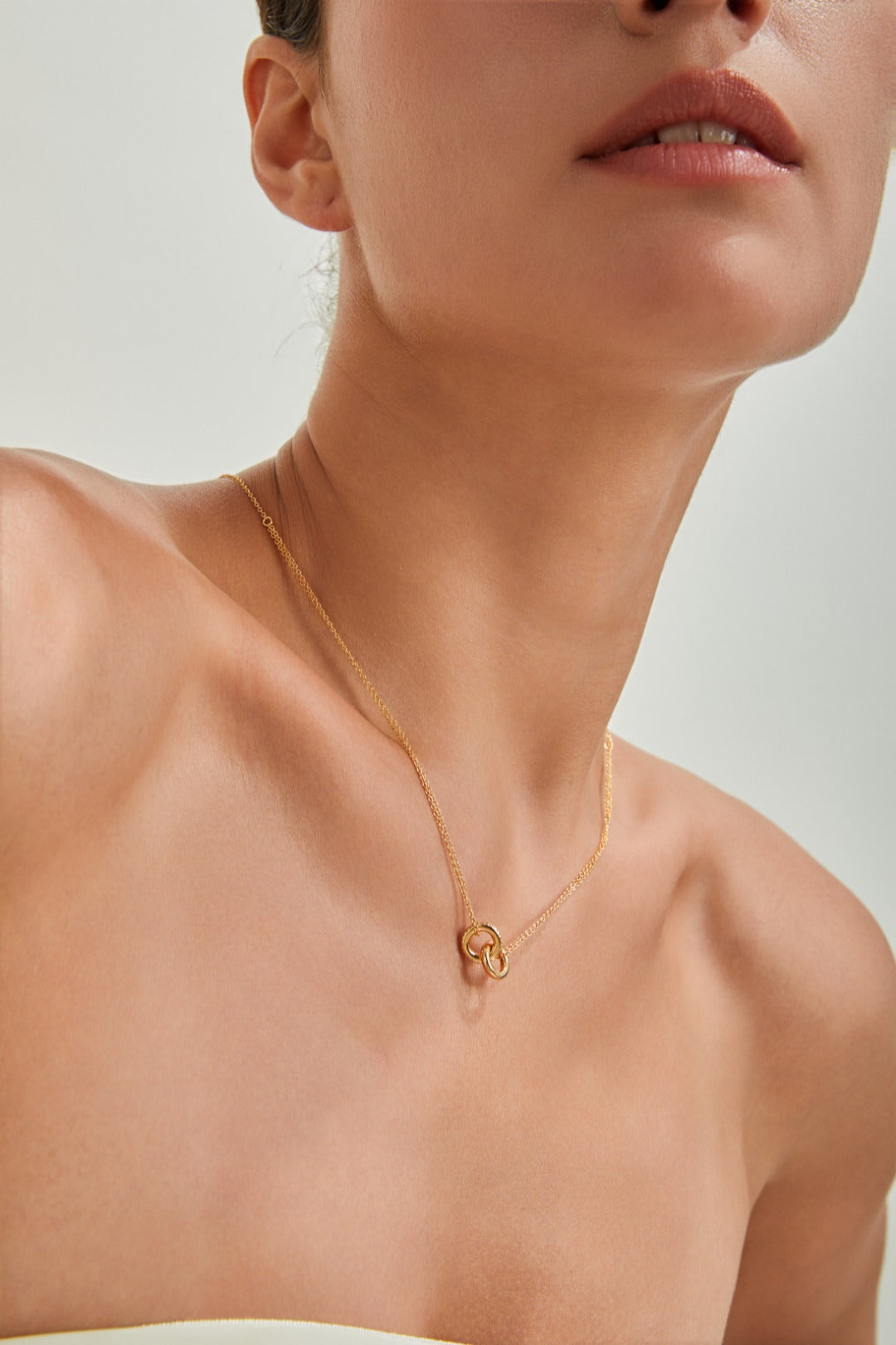 A woman elegantly wears a gold double link necklace adorned with a heart, highlighting her chic fashion sense.
