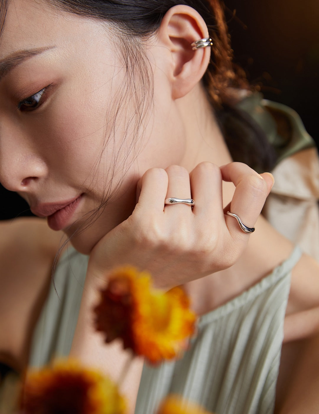 Woman with hand to face, wearing simple silver rings.