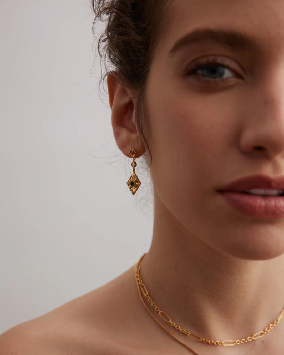 A woman radiating a princess vibe, wearing a gold chain and sparkling earrings.