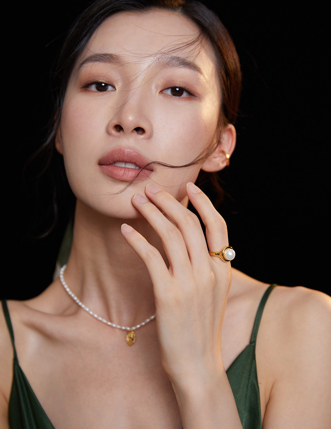 Elegant lady in green dress accessorized with pearl necklace and gold ring.