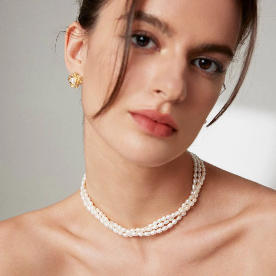 A woman in a triple layer rice pearl necklace and earrings, exuding elegance and charm in her appearance.