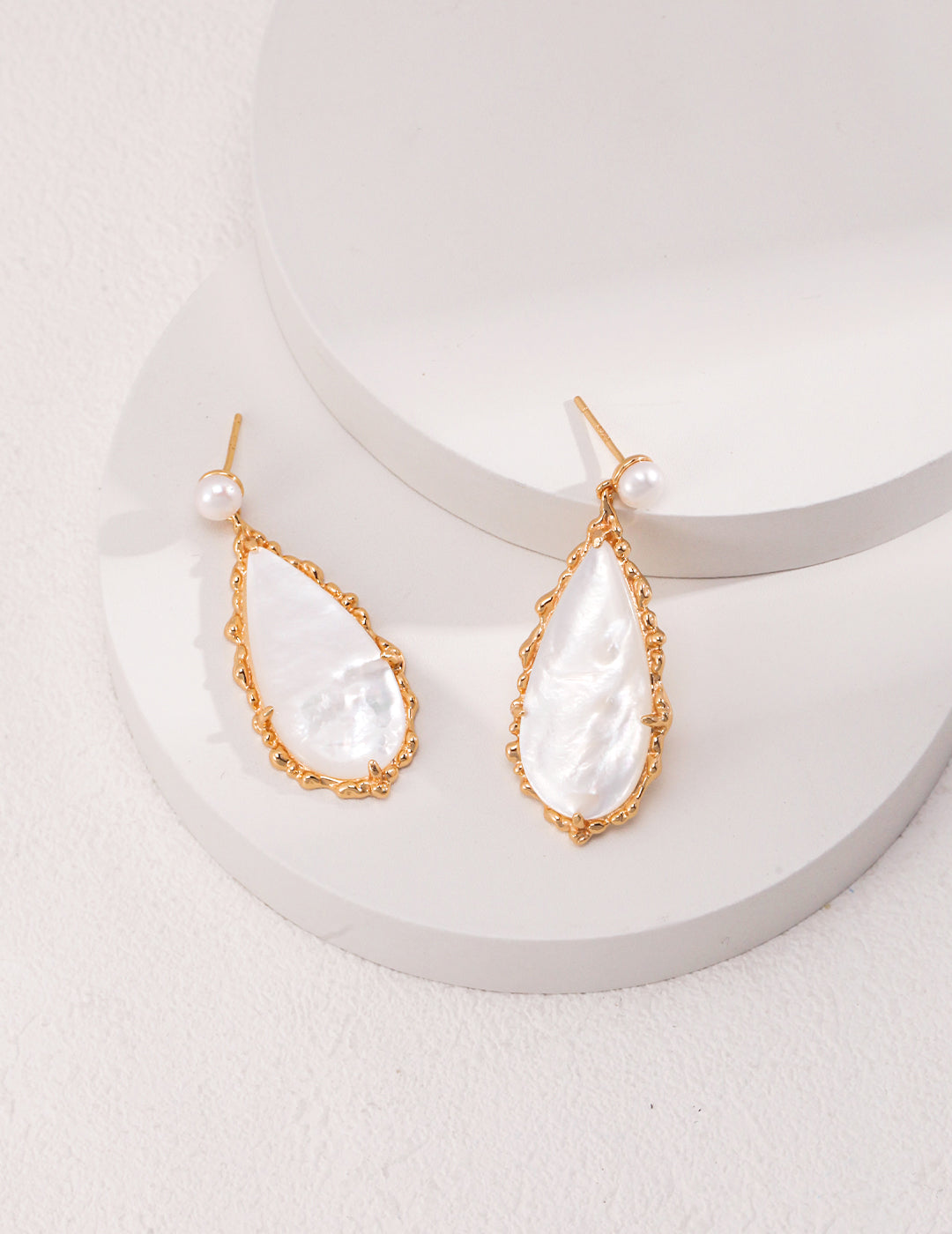 Dazzling gold and white pearl drop earrings elegantly displayed on a pristine white surface.