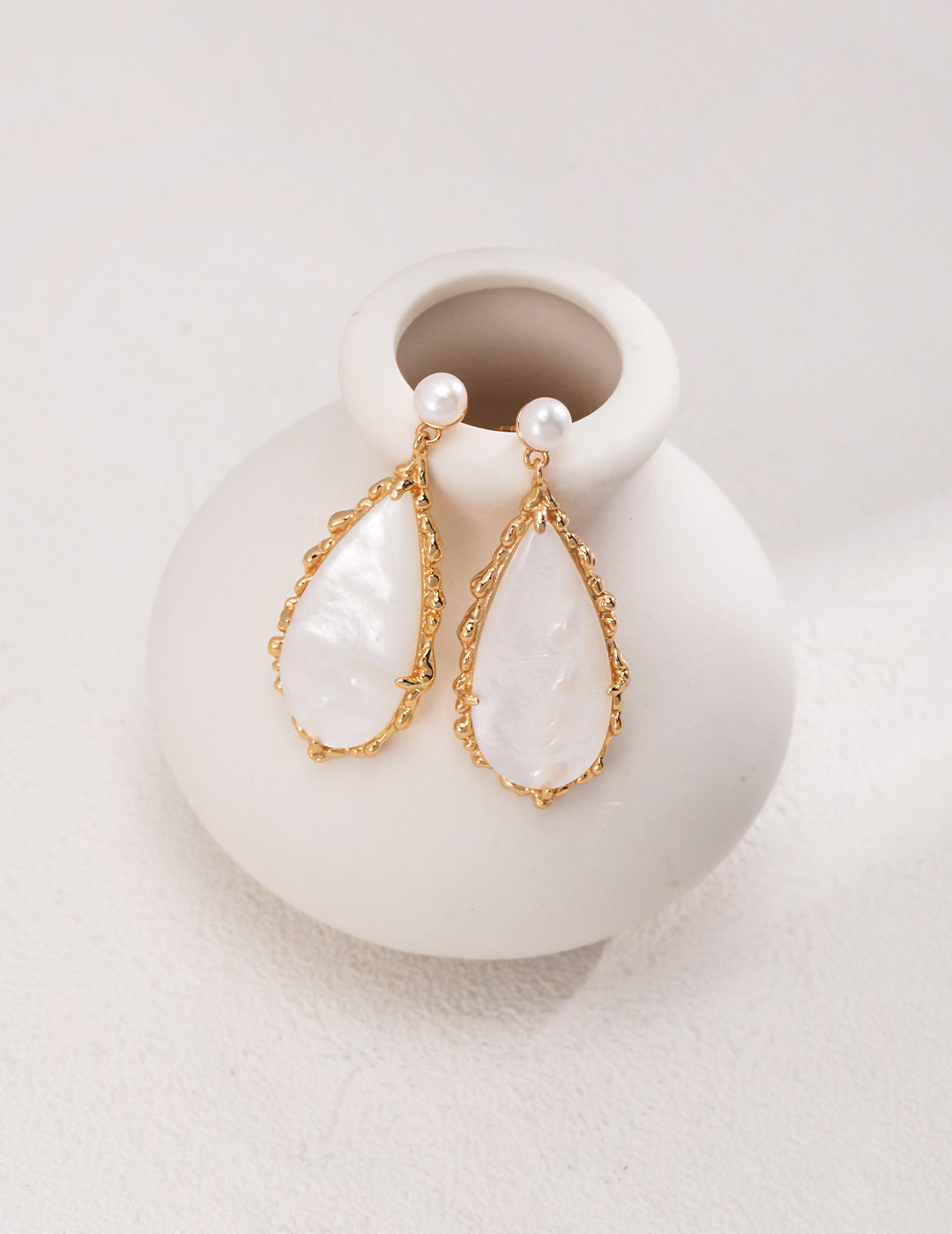 White pearl drop earrings on a gold vase, exuding luxury with their elegant dangles.