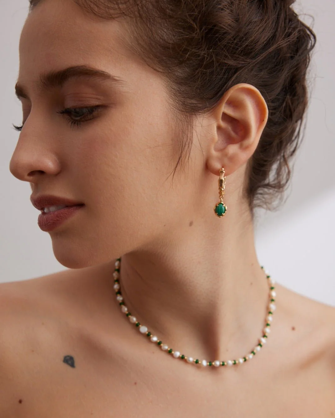 A woman with a green necklace and malachite hoop earrings, emphasizing her fashionable and eye-catching accessories.