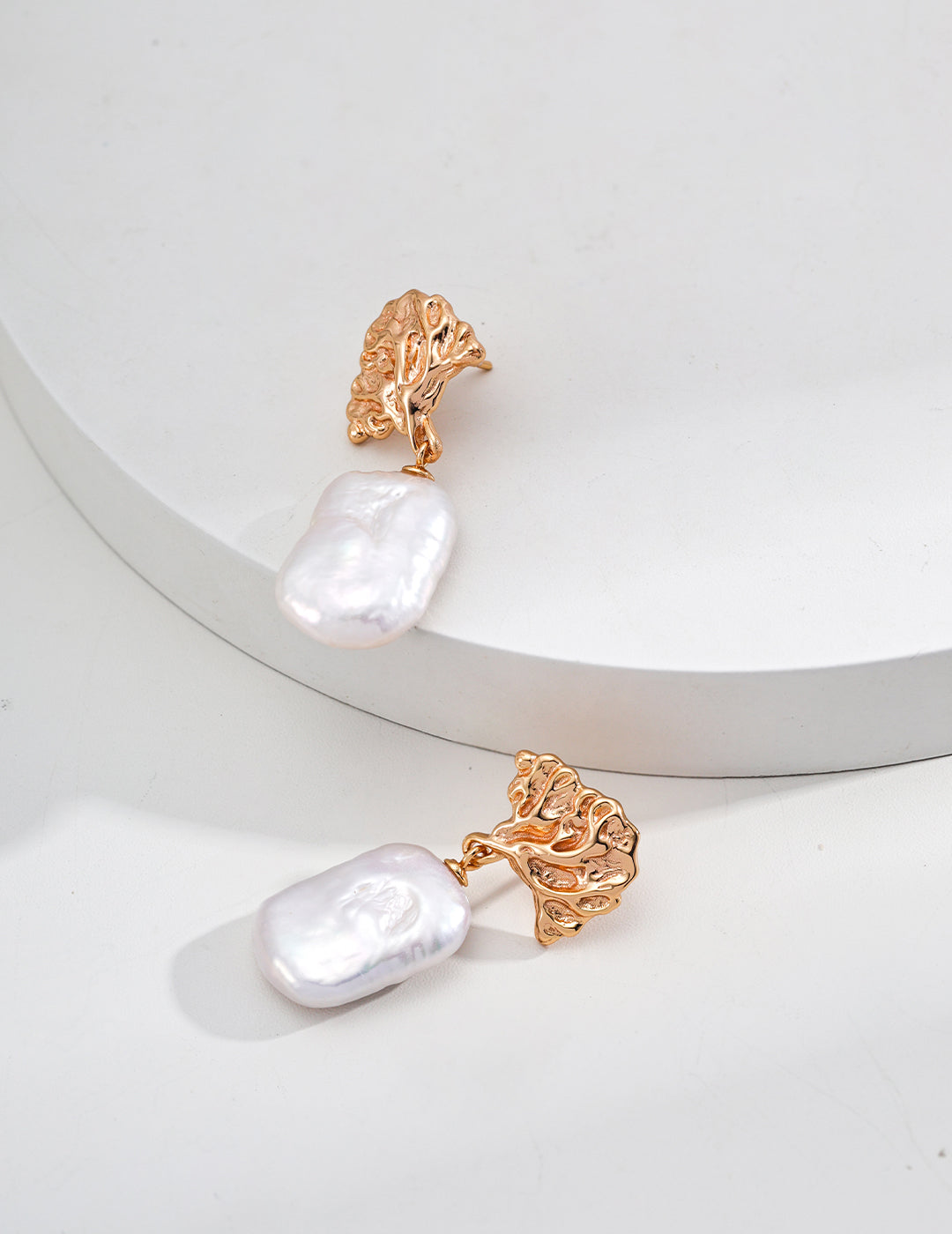 A pair of gold earrings paired with lustrous white pearls, exemplifying elegance and refined style in jewelry design.