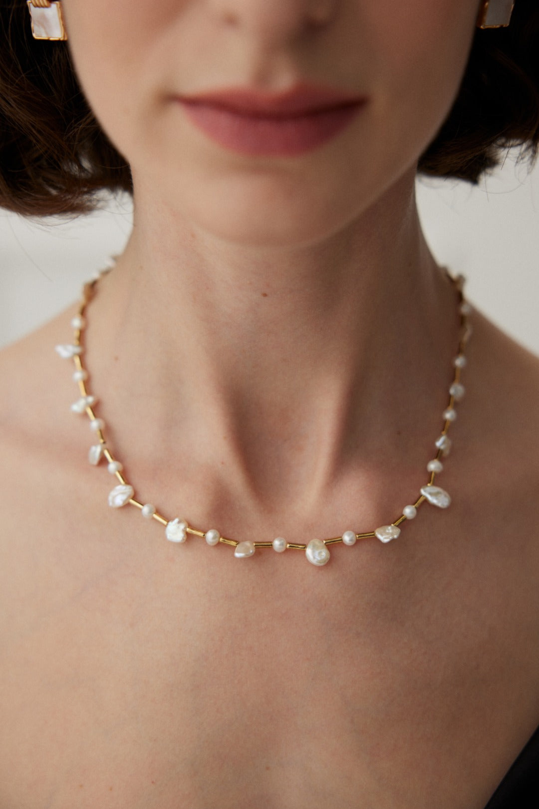 A woman adorned with a pearl necklace and earrings, combining baroque and freshwater pearls for a sophisticated, feminine appearance.