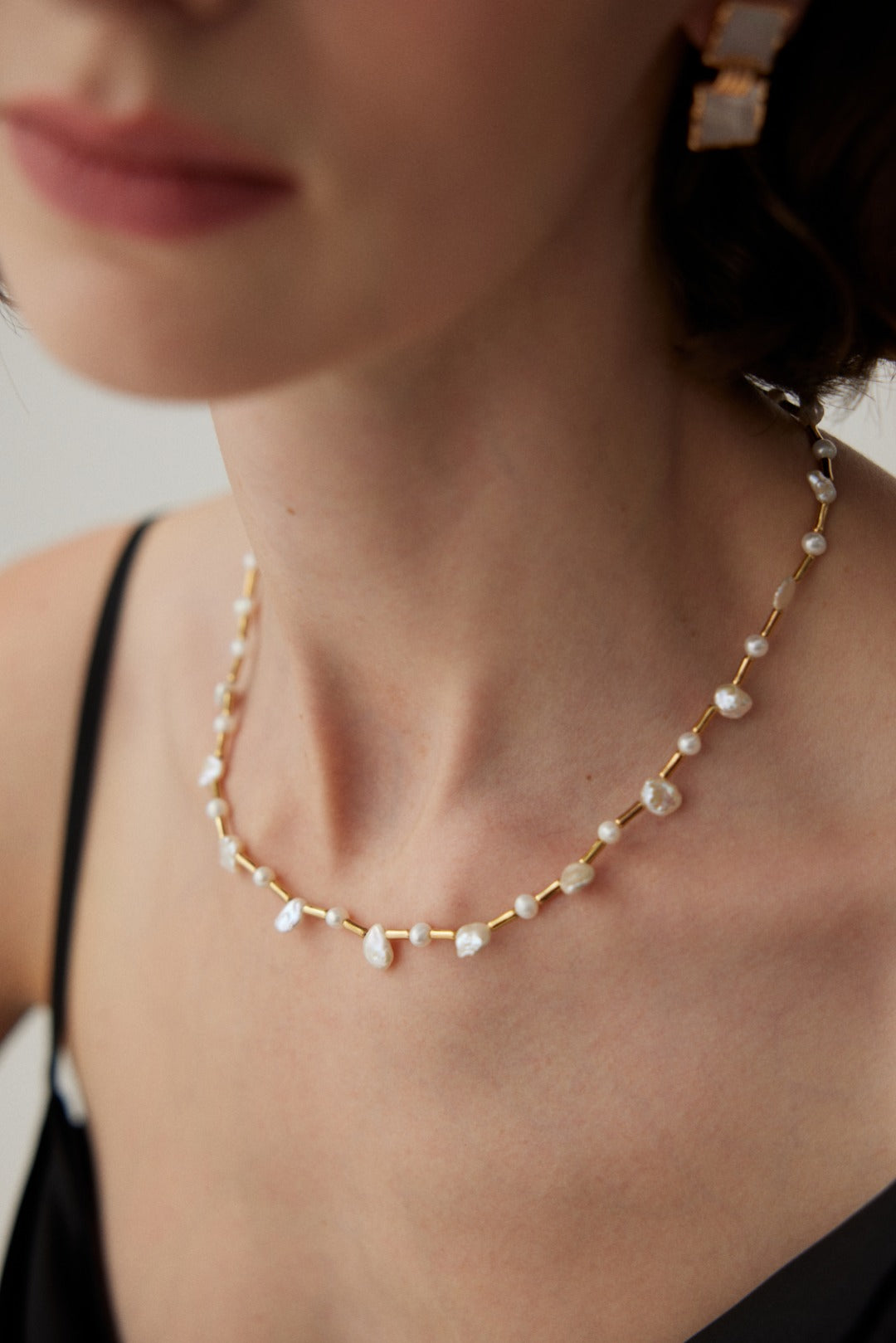 A woman wears a classic gold necklace embellished with baroque and freshwater pearls, exuding timeless elegance.