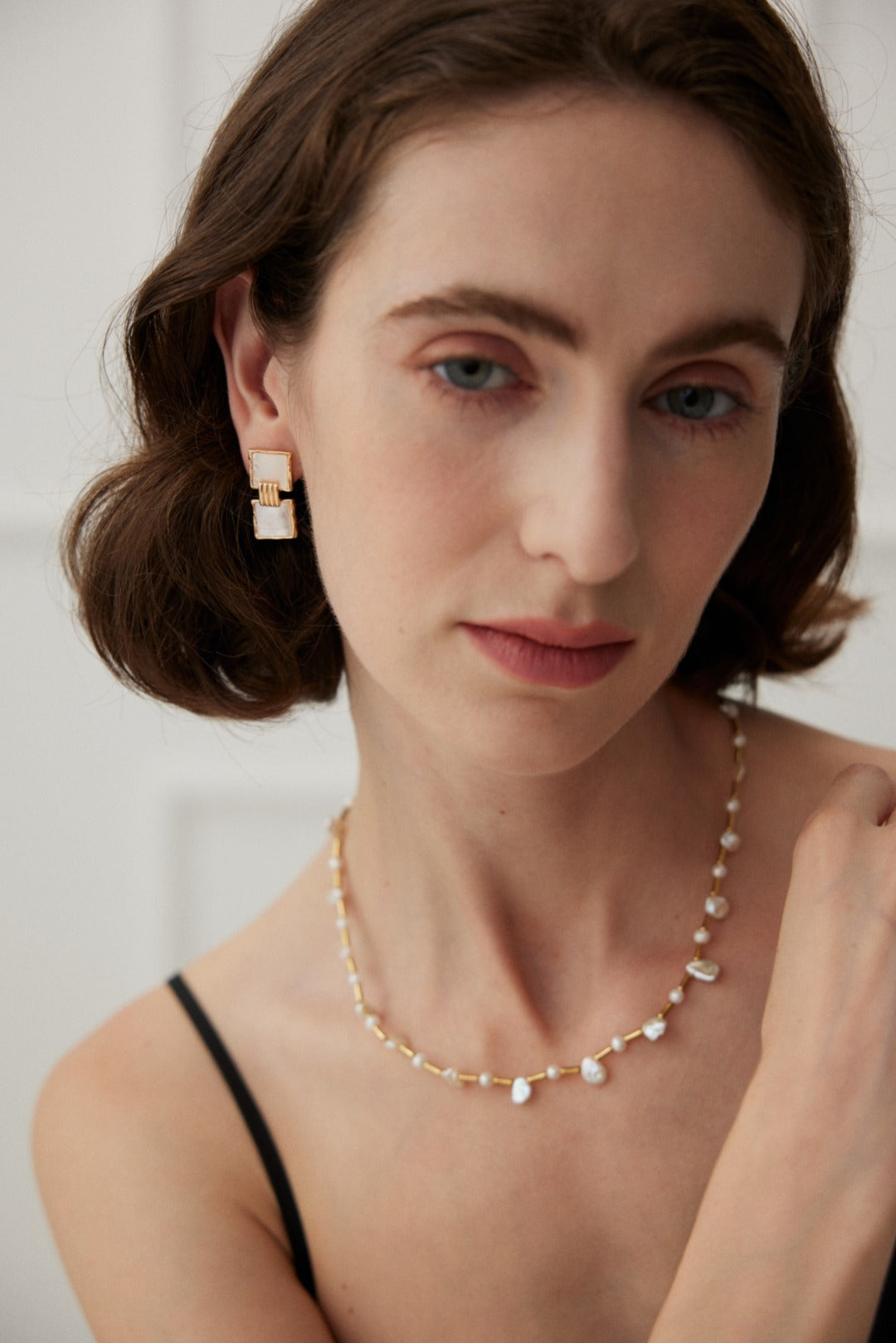A woman showcases an elegant necklace and earrings made of baroque and freshwater pearls, exuding a dreamy vibe.