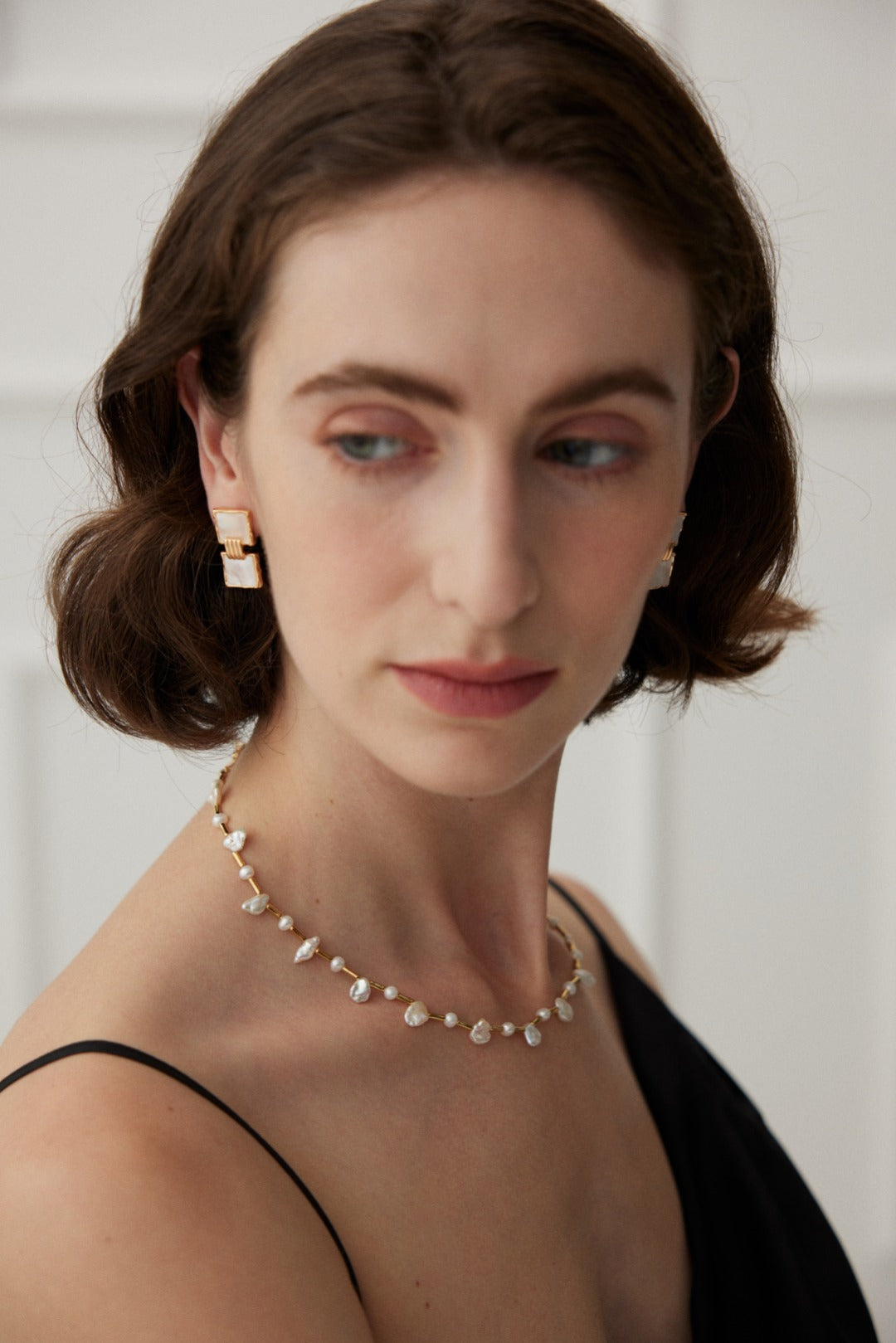 A woman adorned with an elegant necklace of baroque and freshwater pearls, complemented by matching earrings.