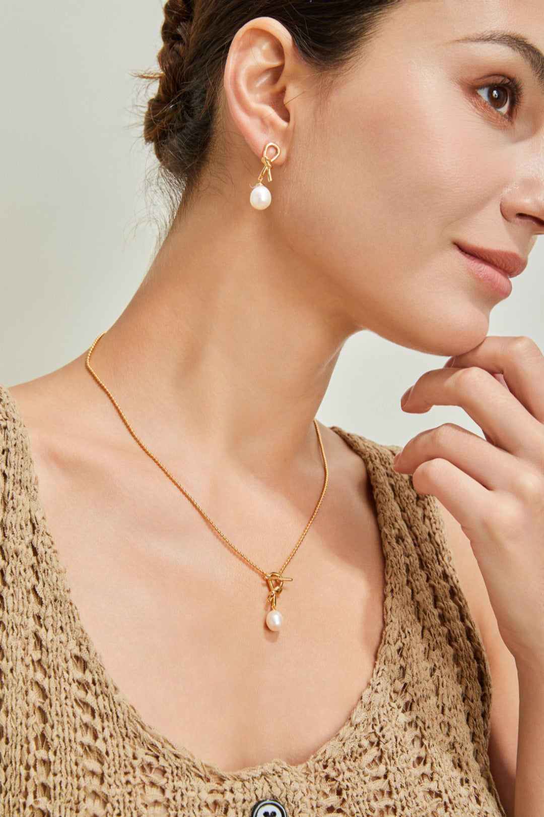 A woman adorned with a beautiful gold knot necklace and earrings, exuding sophistication and charm.