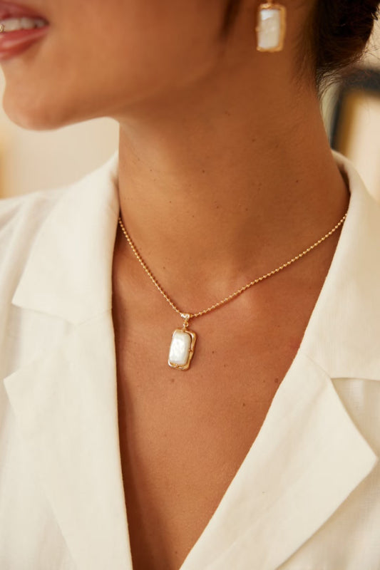 A woman dressed in a white shirt adorned with a freshwater pearl necklace and a gold necklace, exuding elegance.