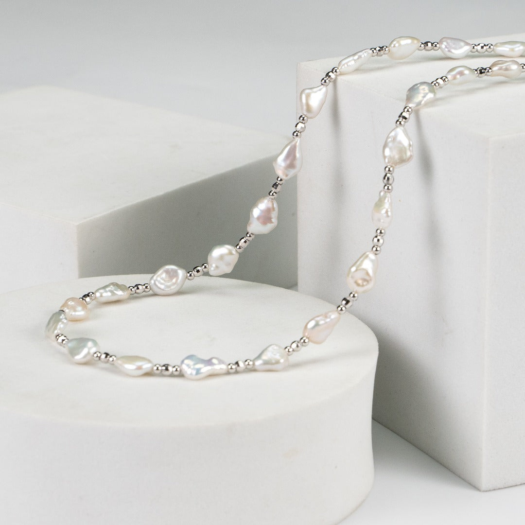 Luxurious white baroque pearl necklace resting on a white marble table, highlighting its elegance and refined beauty.