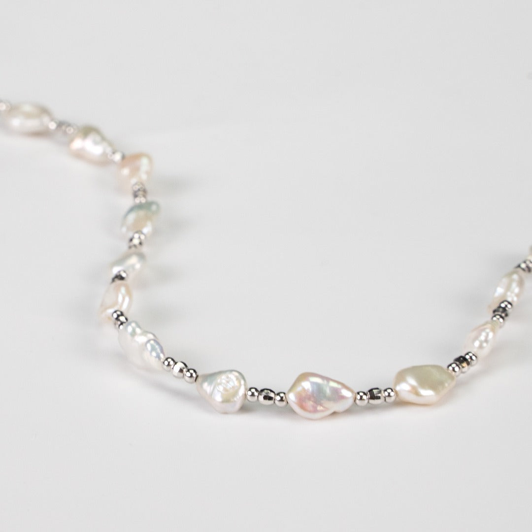 Detailed view of a white baroque pearl necklace featuring silver beads, highlighting its luxurious and classic appeal.