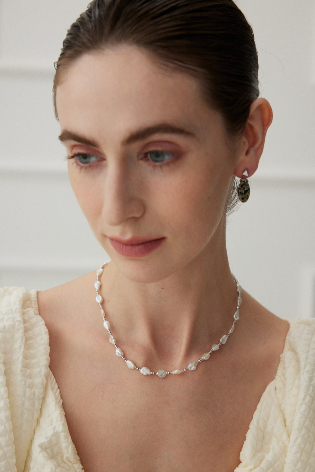 Close-up of a woman in a white dress, showcasing a baroque pearl necklace, exuding a feminine elegance.