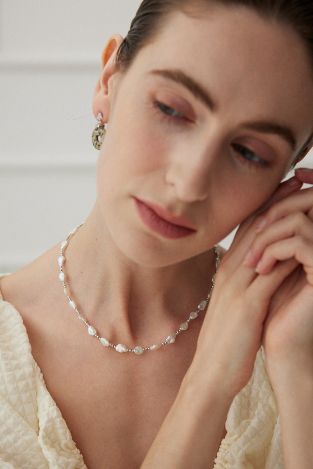 Close-up of a smiling woman adorned with a feminine necklace featuring lustrous baroque pearls.