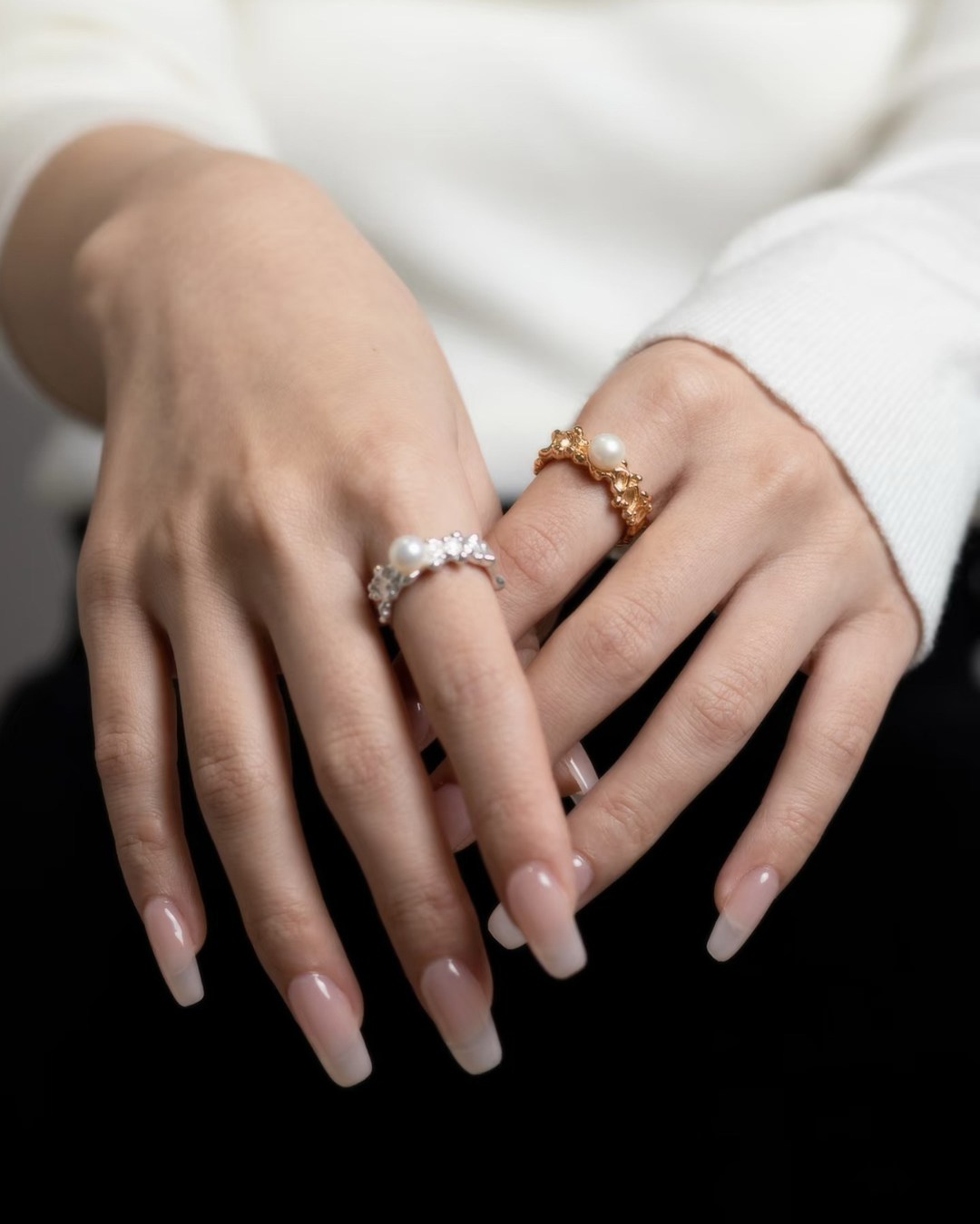 Lifestyle photograph of a model's hands wearing two Harper ringsāone in textured silver and one in textured goldāfeaturing an open band style with prominent pearl details.