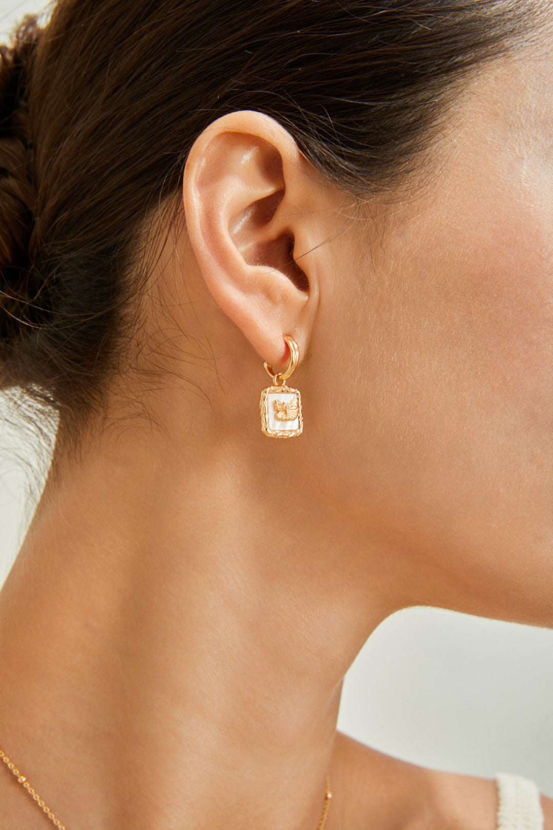 A model wears stunning square gold earrings featuring butterfly nacre, combining modern design with classic elegance.
