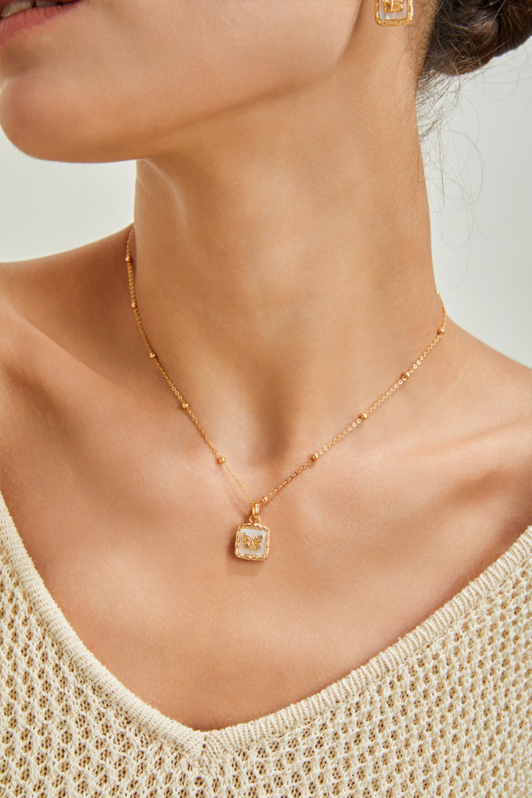 A woman showcases a nacre butterfly necklace and gold earrings, highlighting her chic and sophisticated style.