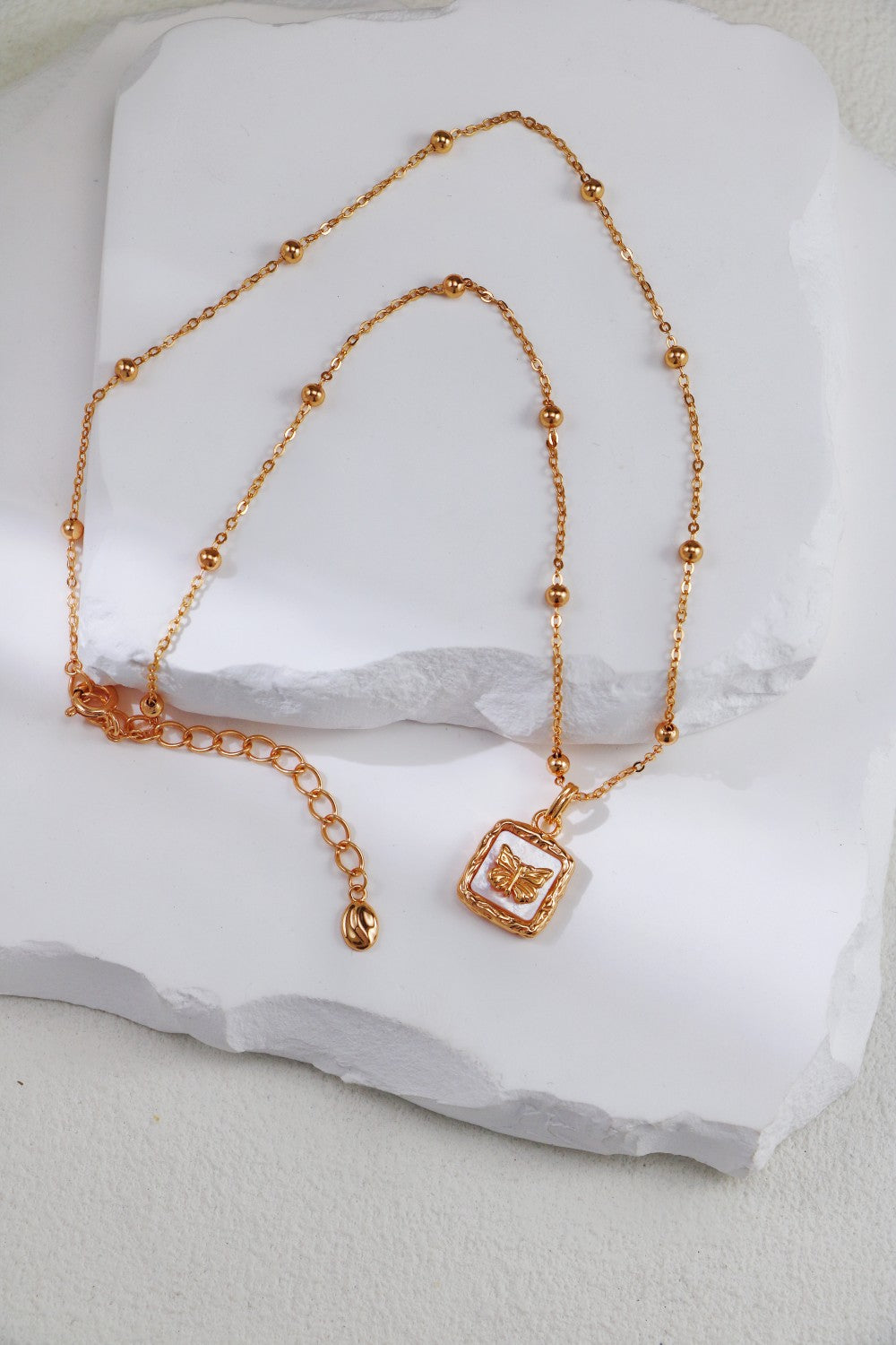 Stunning gold necklace with a square pendant, highlighted by a delicate nacre butterfly, perfect for any occasion.