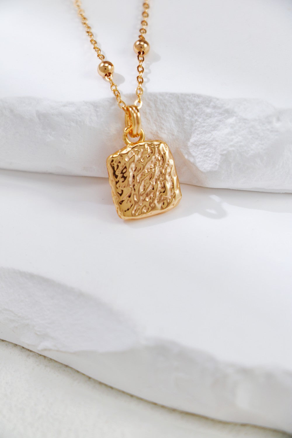 Gold-plated square pendant necklace on a white surface, featuring the detailed back of a nacre butterfly design.