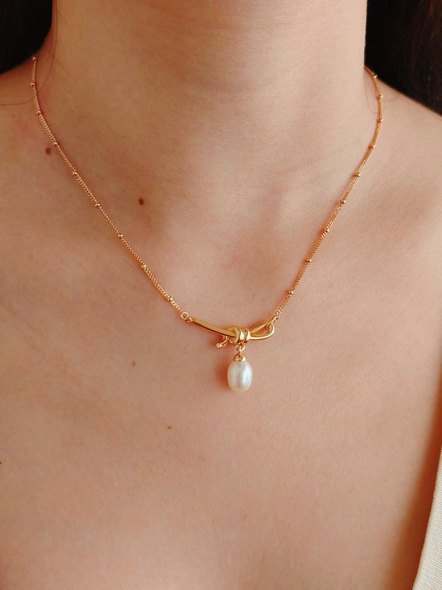A woman wears a chic gold necklace with a single pearl, adding a touch of elegance to her overall look.