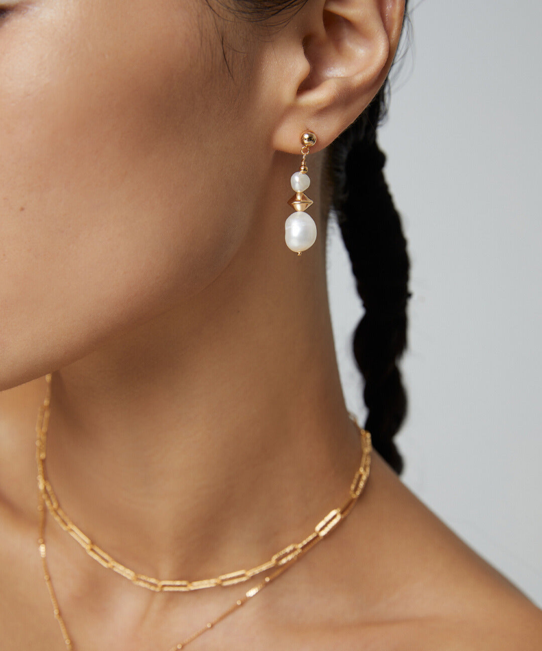 A woman wearing gold dangling earrings with baroque pearls.