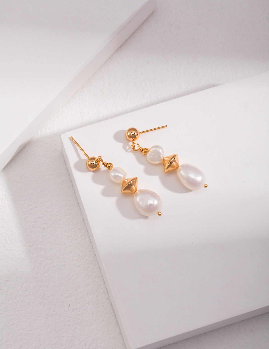 Elegant gold and white pearl earrings on white background.