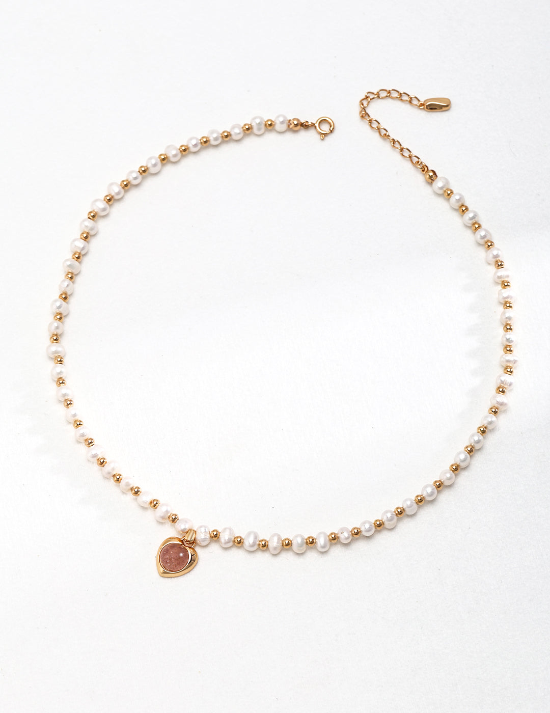 Elegant gold necklace featuring a pink heart charm, pearls, and strawberry quartz.