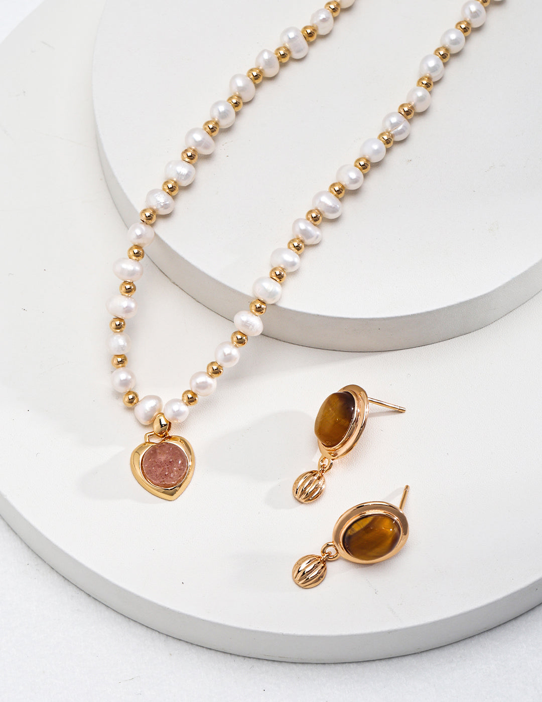 Stunning gold necklace adorned with heart-shaped strawberry quartz and pearls, complemented by tiger's eye earrings.