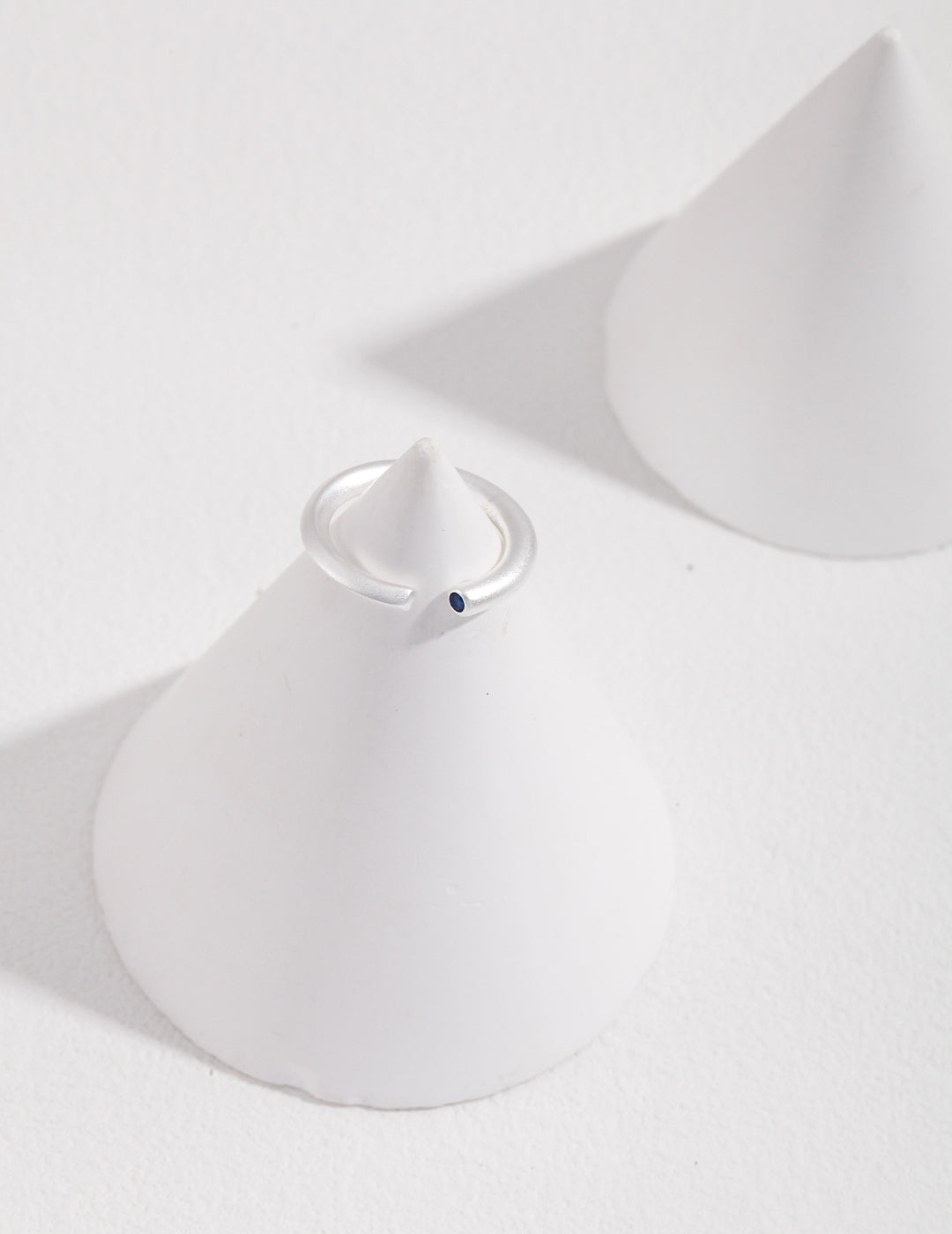 A minimalist silver ring on a white cone featuring an aquamarine stone.