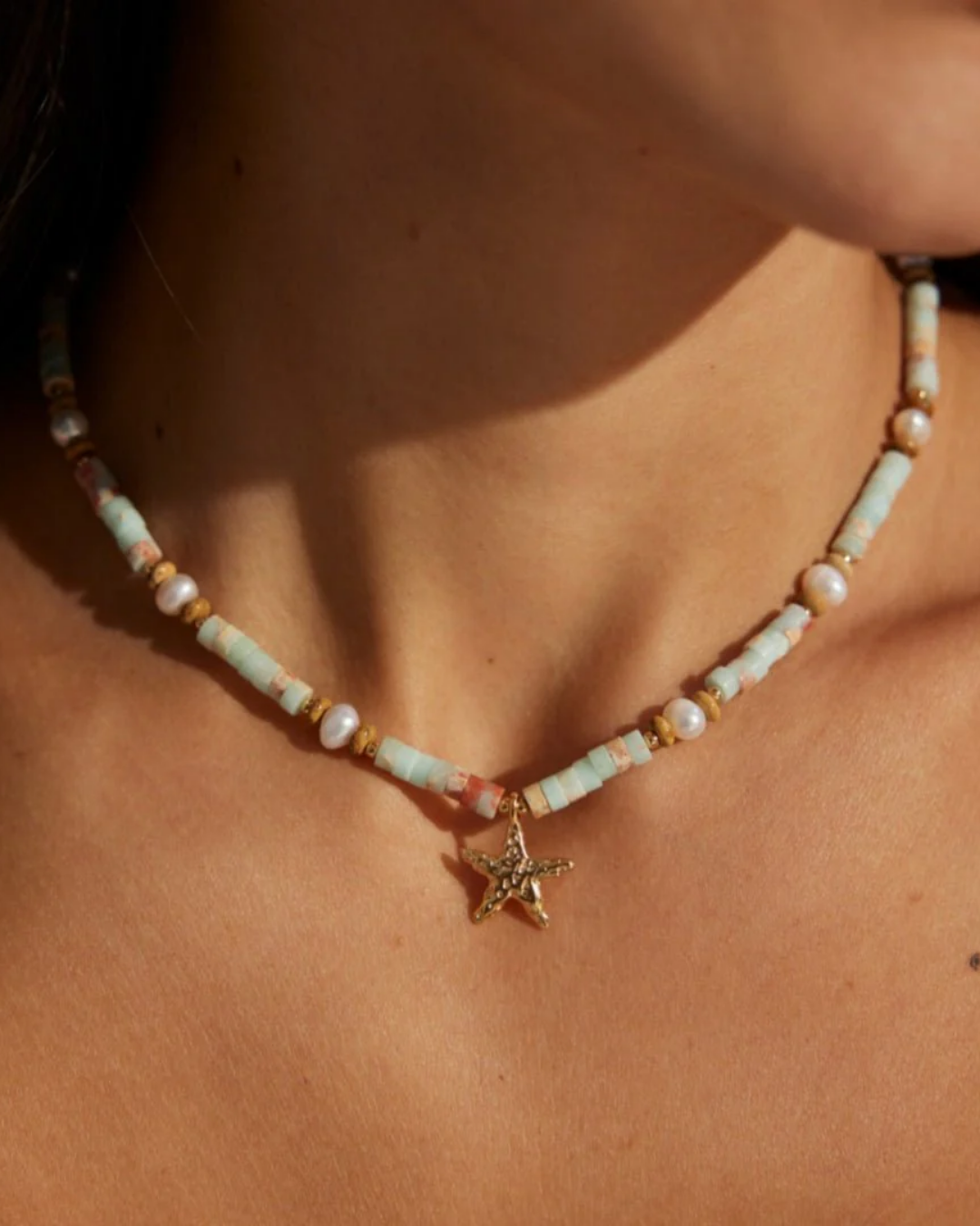 Close up of a woman wearing a necklace with a gold starfish charm, emphasizing her fashionable look and love for ocean-themed accessories.