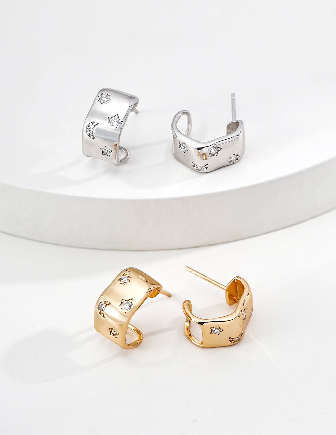 Two pairs of C-Shaped Hoops, one in silver, one in gold, embellished with small zirconia on white background