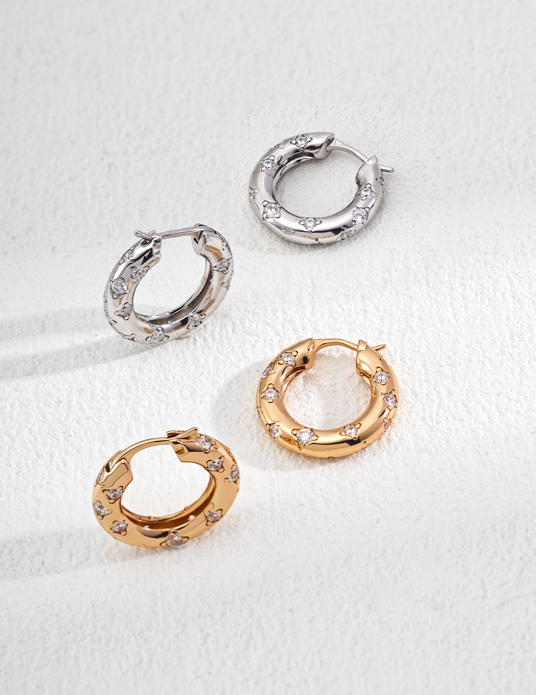 A collection of unique gold and silver hoop earrings, highlighting their diverse styles and shimmering materials.