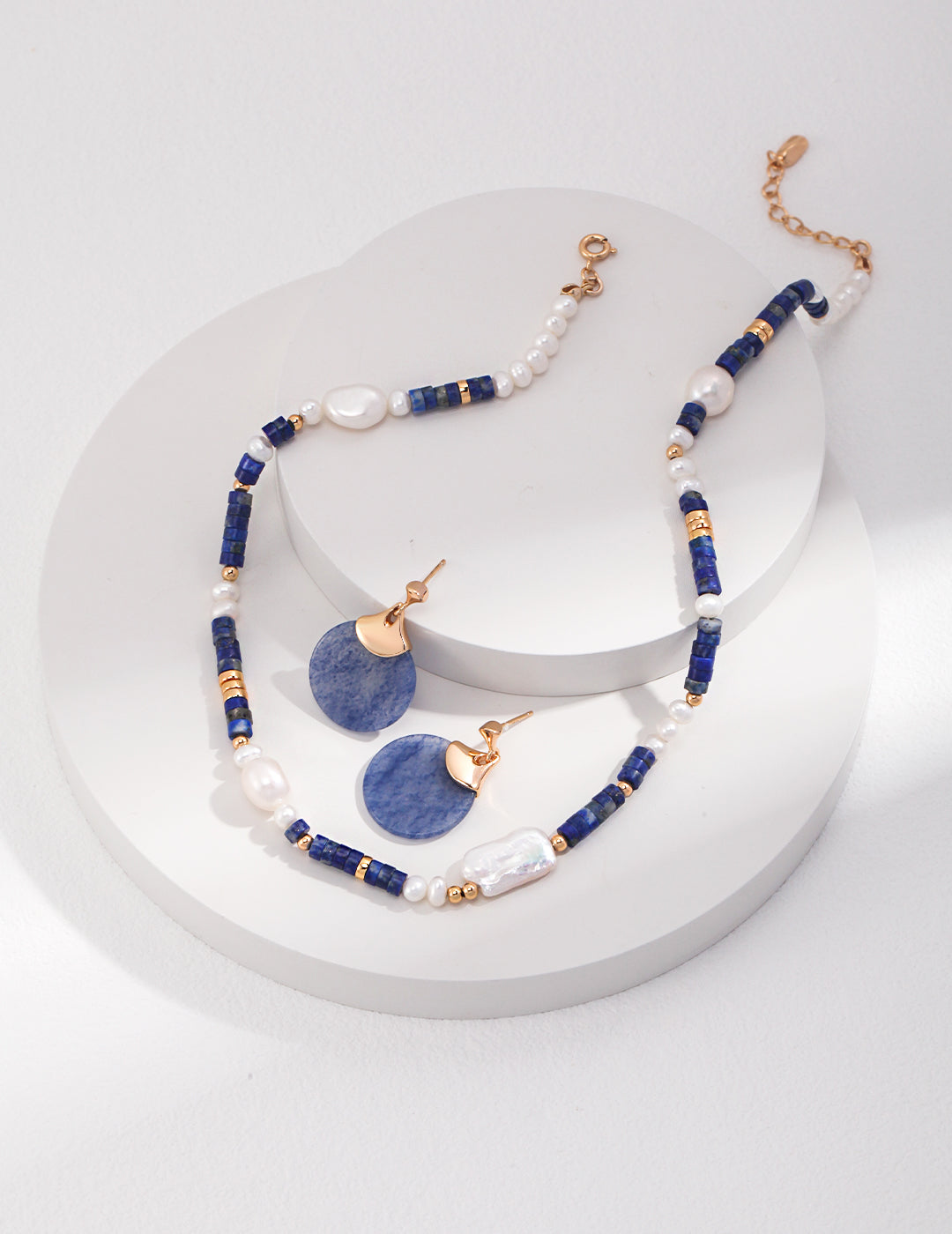 Blue lapis lazuli necklace and earrings set with freshwater pearls on white surface.