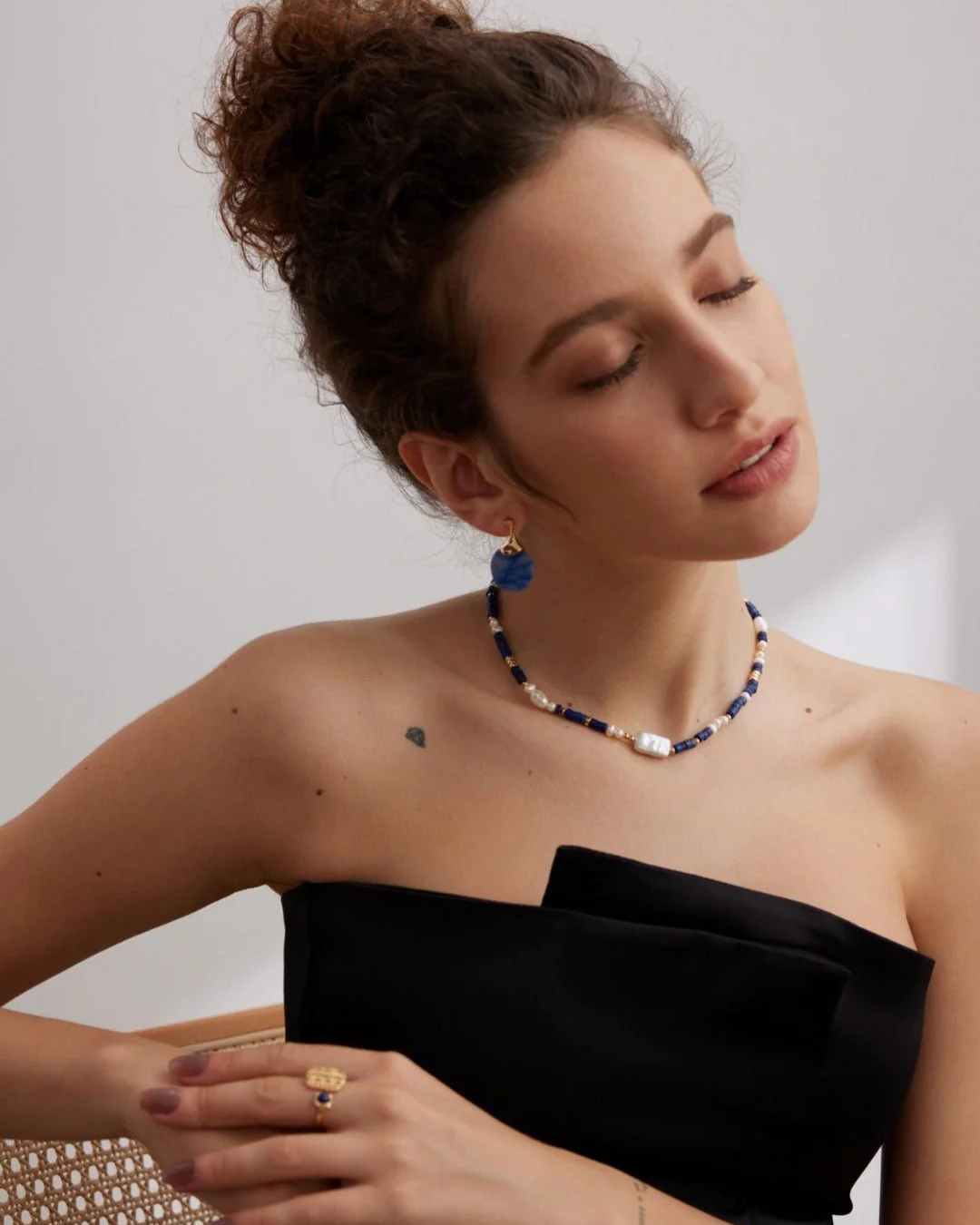 A woman in a stylish black dress adorned with a vibrant blue necklace, exuding elegance and confidence.