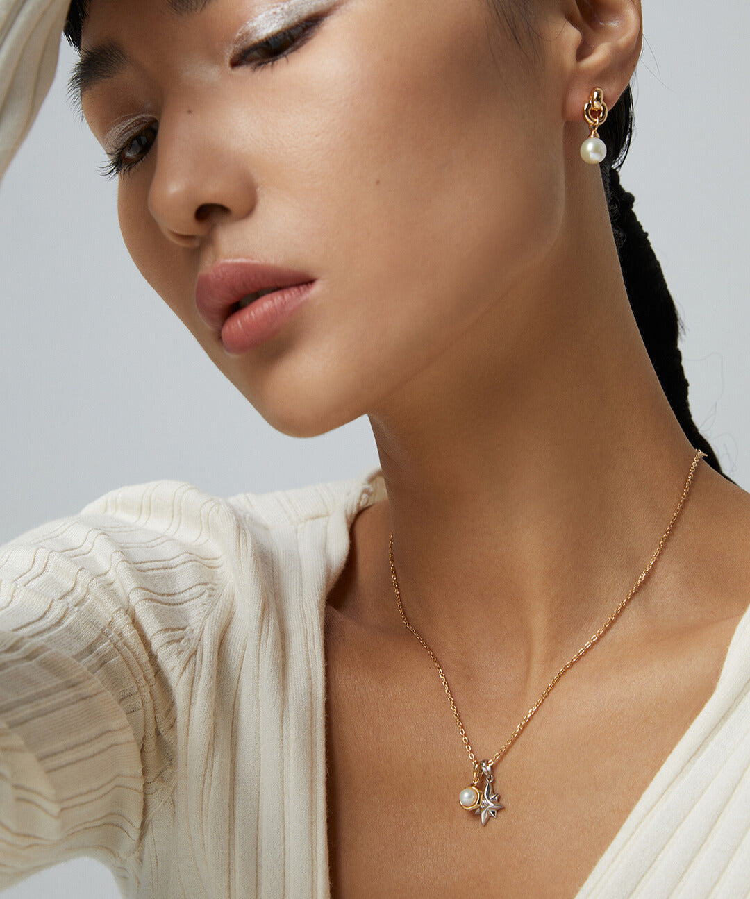 A woman in a white sweater wearing a gold necklace with celestial charms.