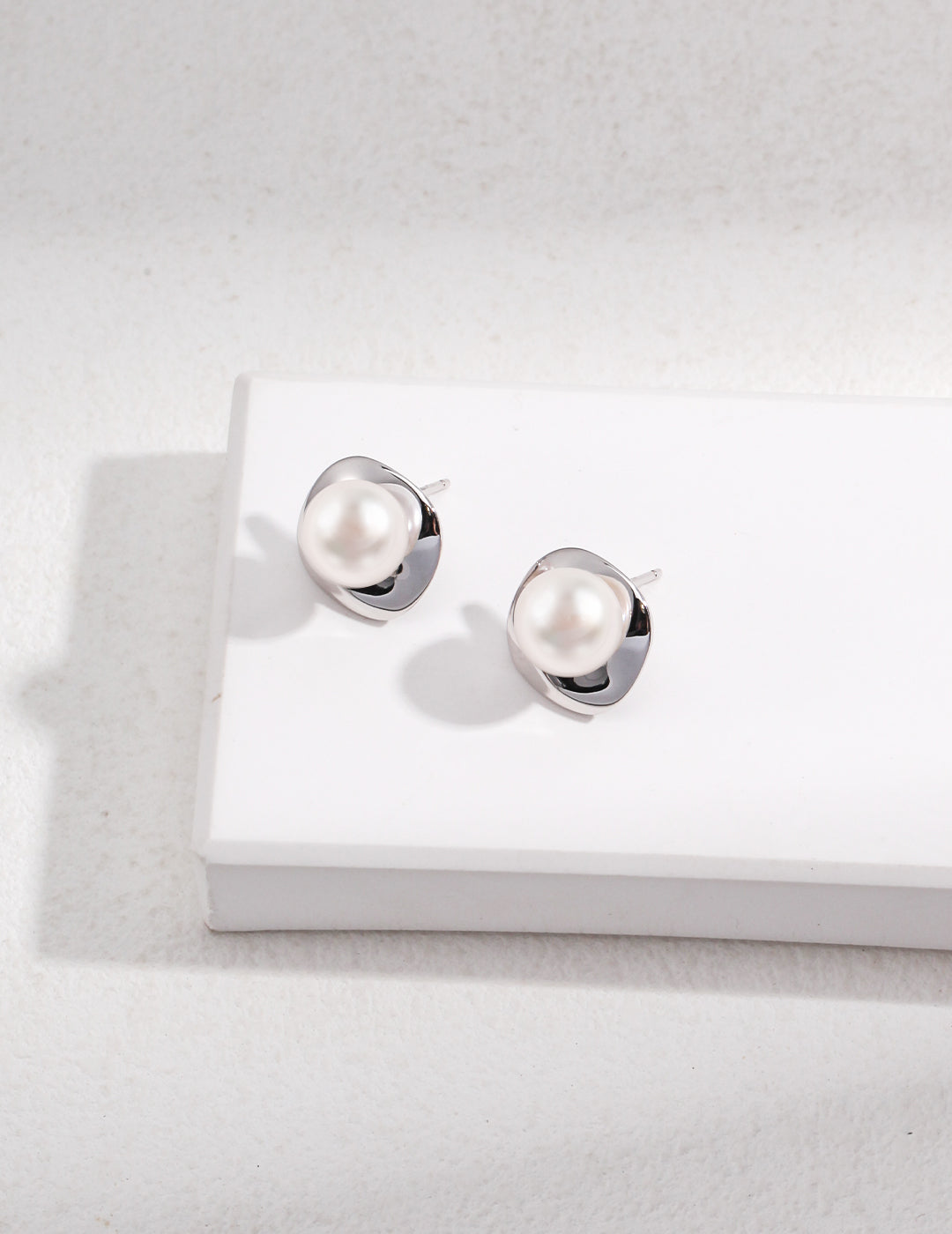 Stylish white pearl studs on white surface, silver plated finish.