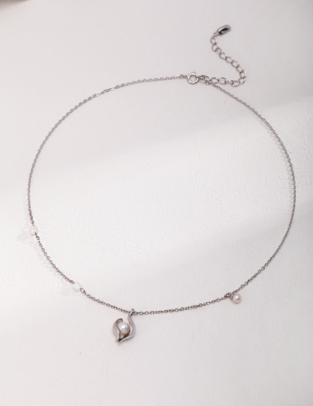A silver necklace with a heart charm, featuring a nacre freshwater pearl in a shell pendant.
