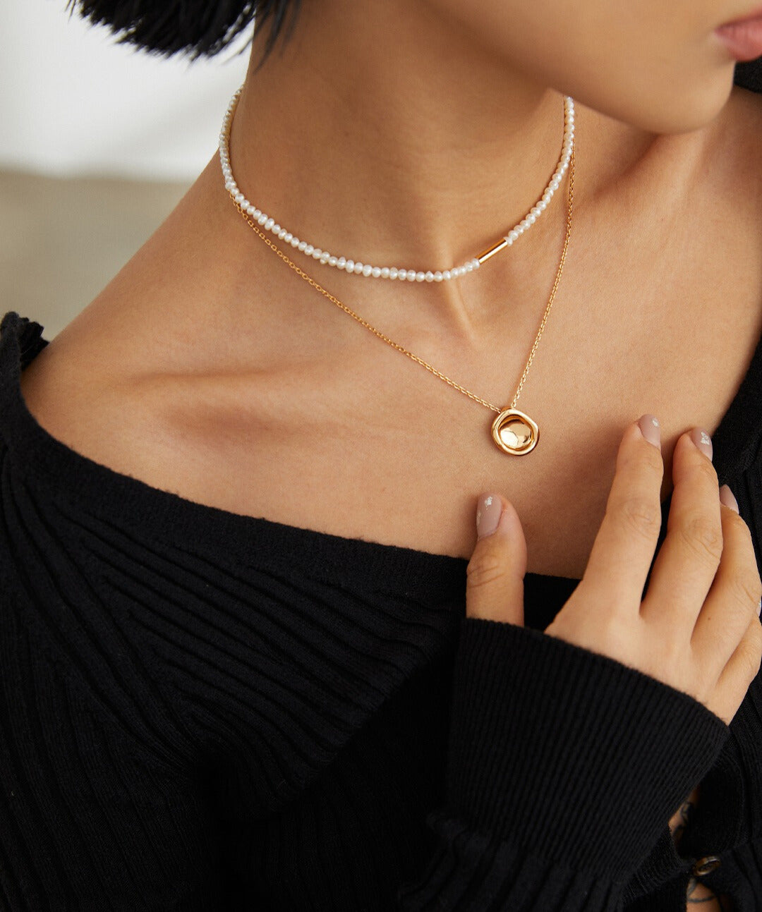 A woman model adorned with a gold necklace and a pearl necklace, exuding grace and style.