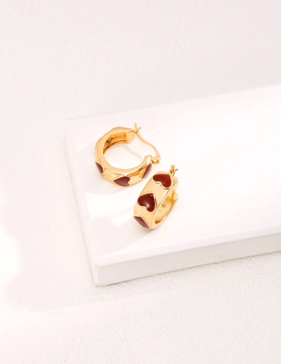 Stylish gold hoop earrings, featuring cute red enamel hearts.
