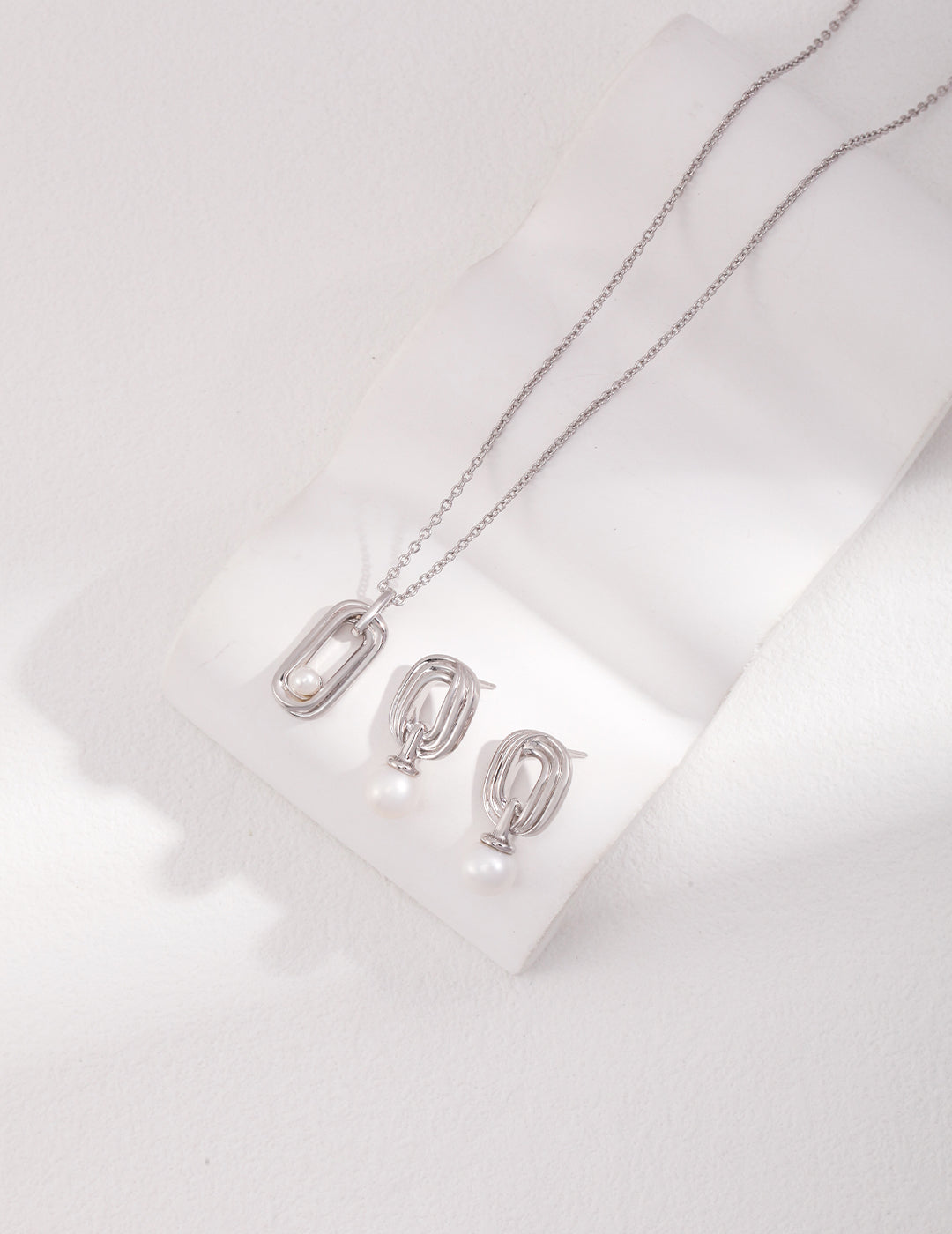 Silver freshwater pearl necklace and matching earrings on white surface.