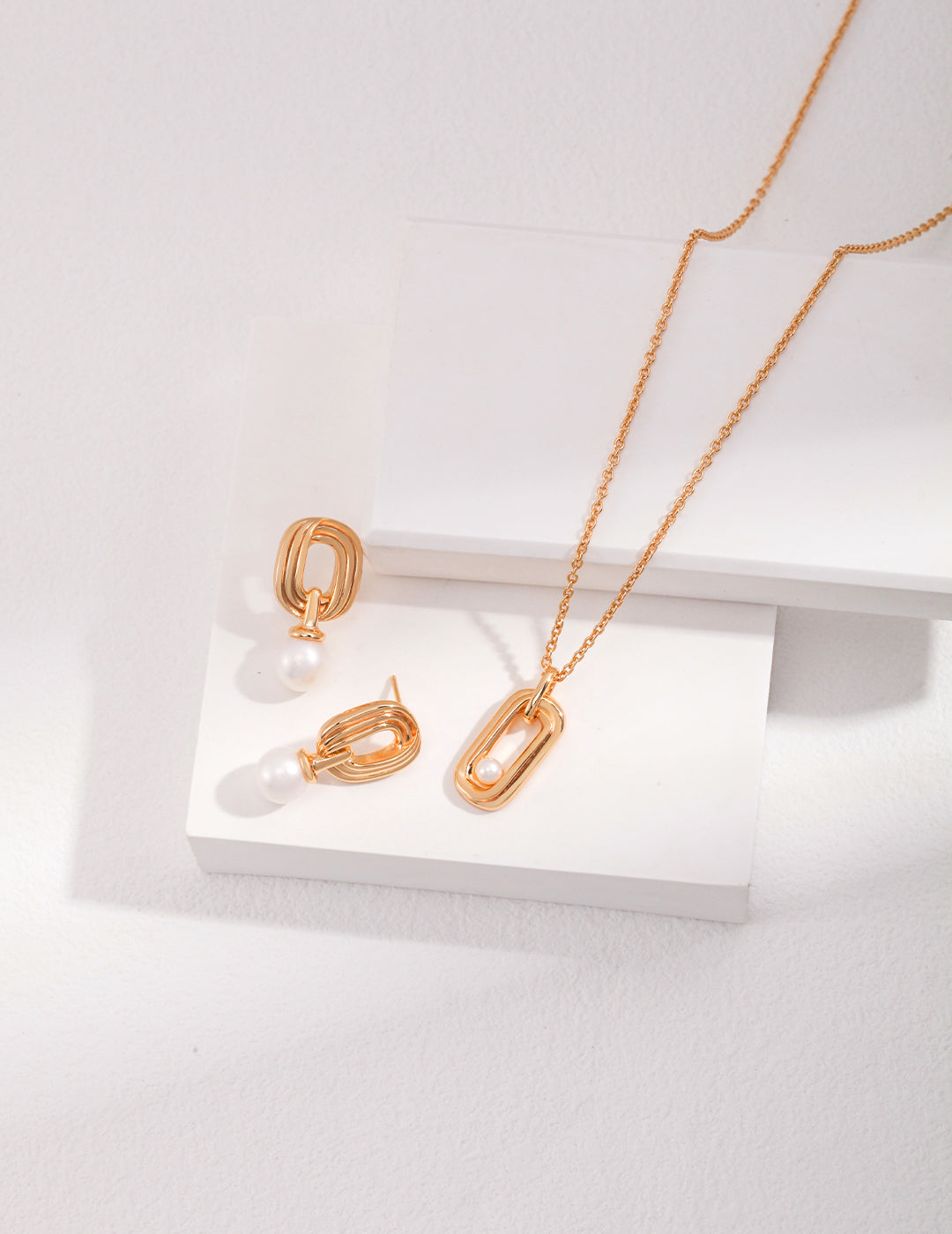 Stylish gold necklace and earrings with freshwater pearls on white.
