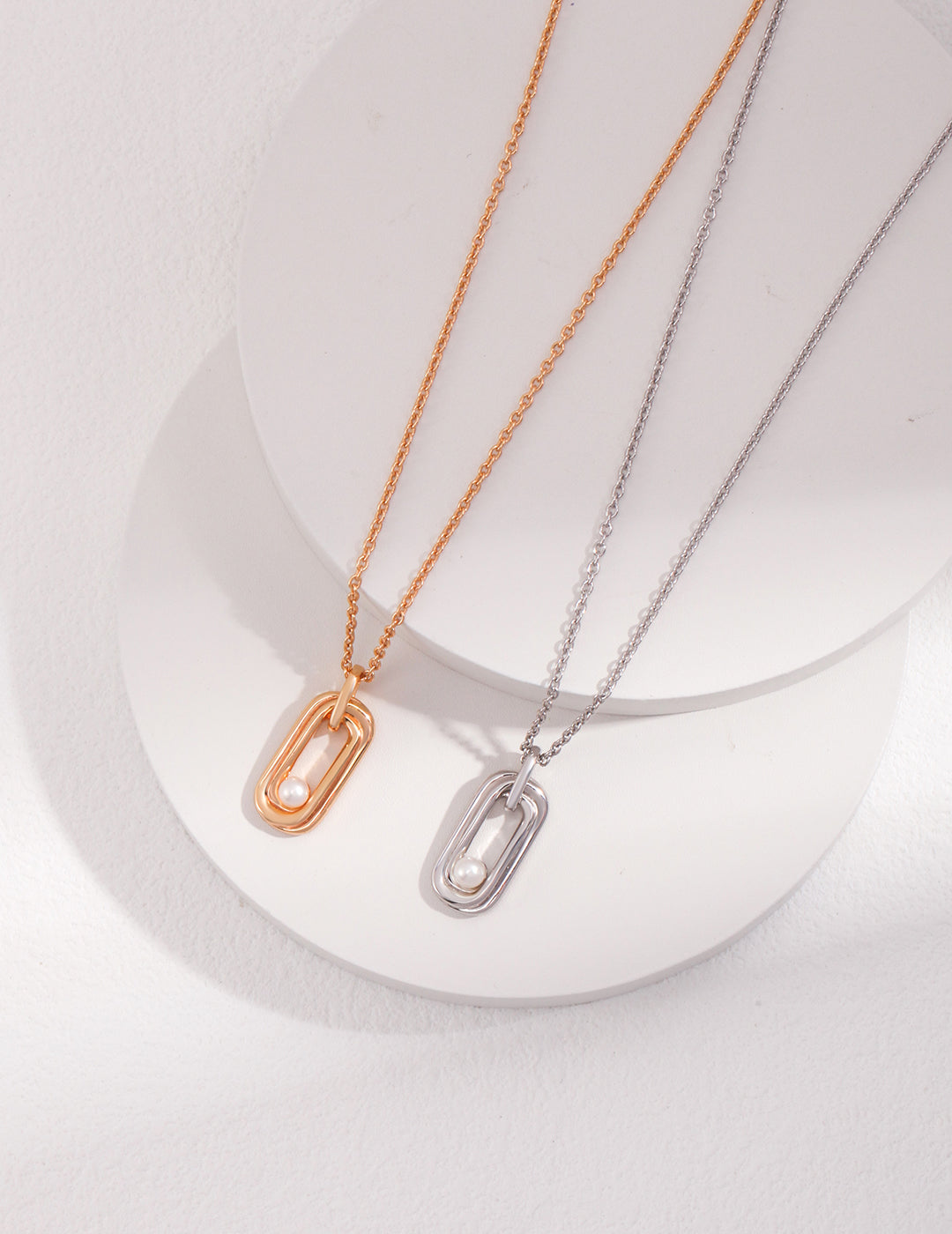 Two elegant necklaces with small oval pendants, one in gold and the other in silver, adorned with silver and gold freshwater pearls.