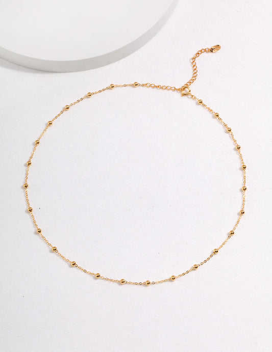 A gold chain necklace with beads interspersed, displayed on a white surface.