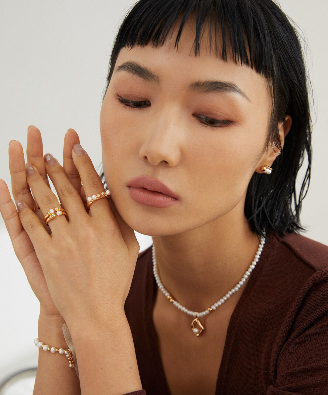 A model wearing gold jewelry, including a necklace and rings adorned with dainty beads and freshwater pearls.