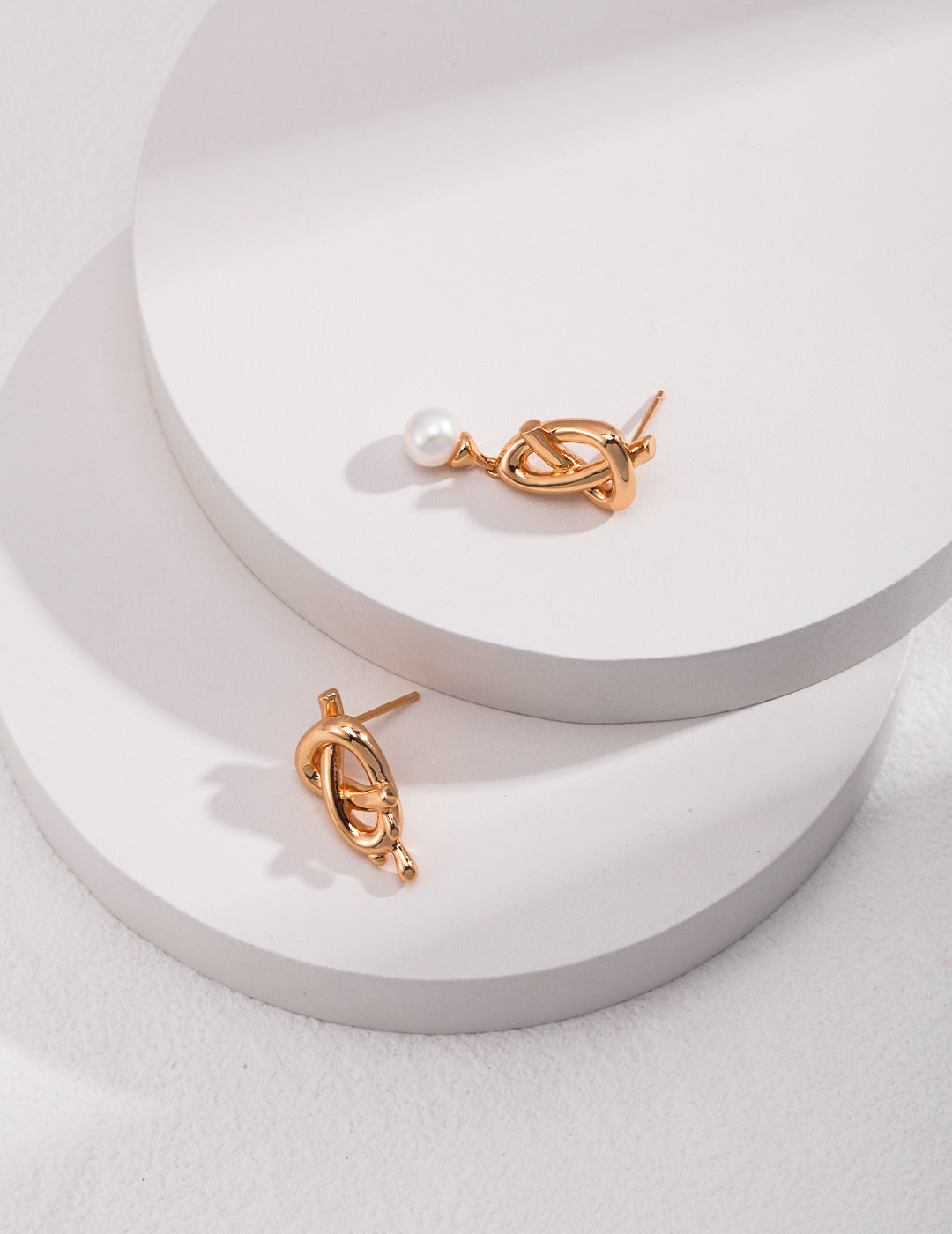 Two gold plated asymmetric earrings with freshwater pearls on top of a white surface.