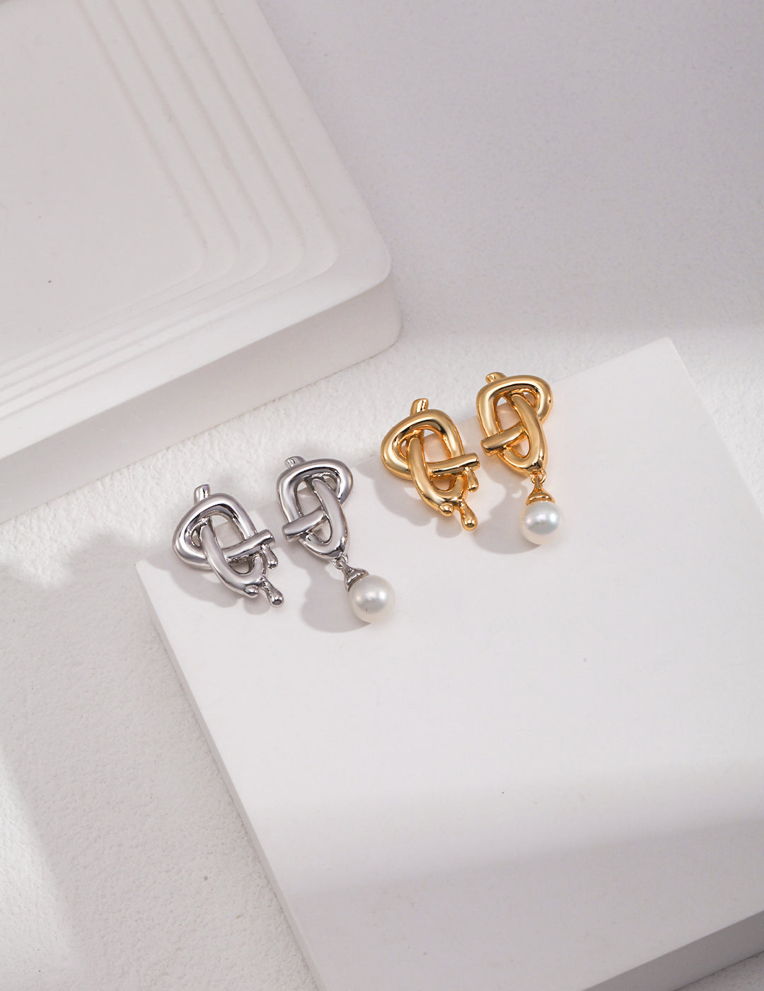 Two pairs of gold and silver earrings with a pearl, featuring asymmetric designs.