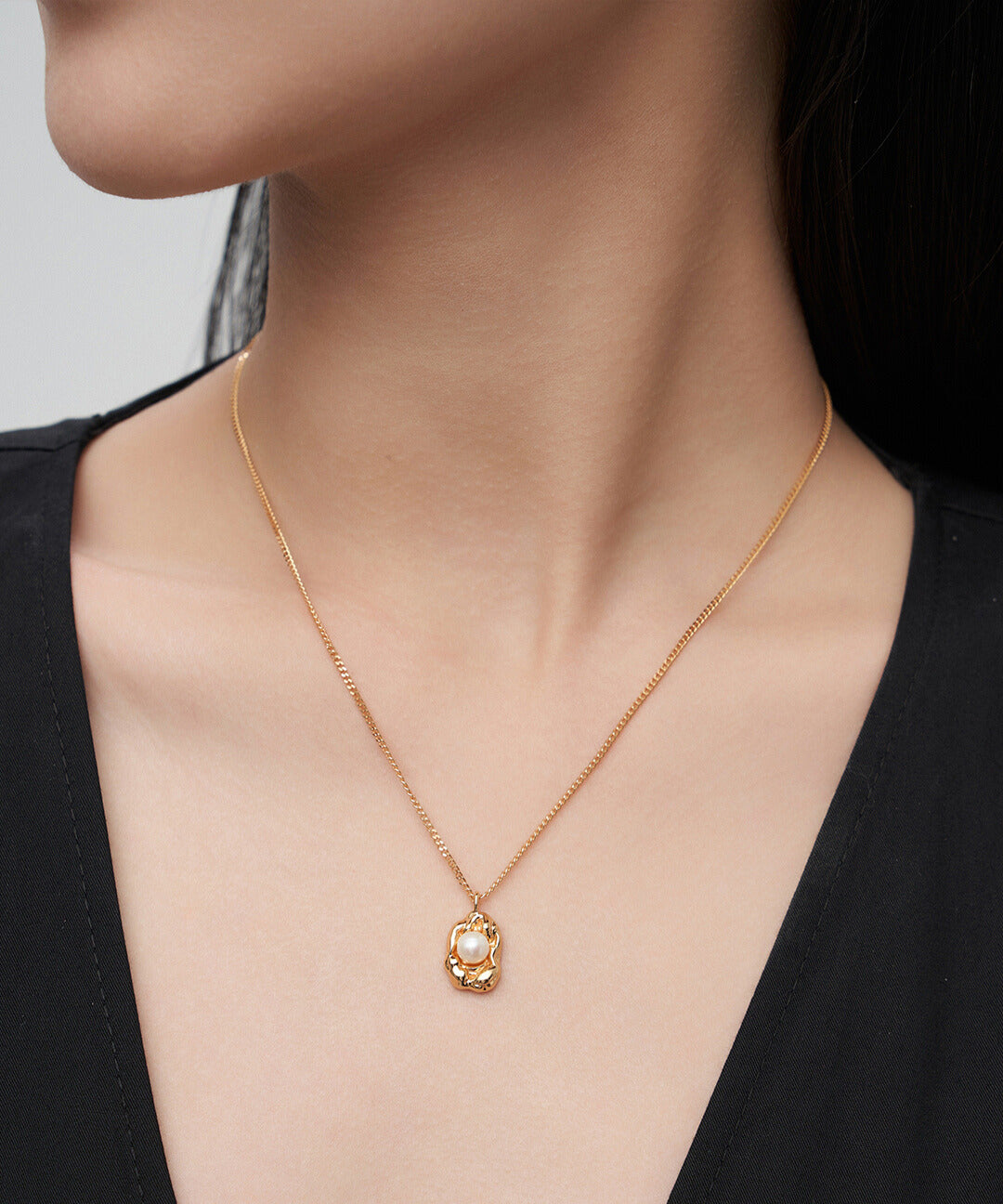 Gold plated necklace with small flower charm, adorned with freshwater pearl, worn by model.