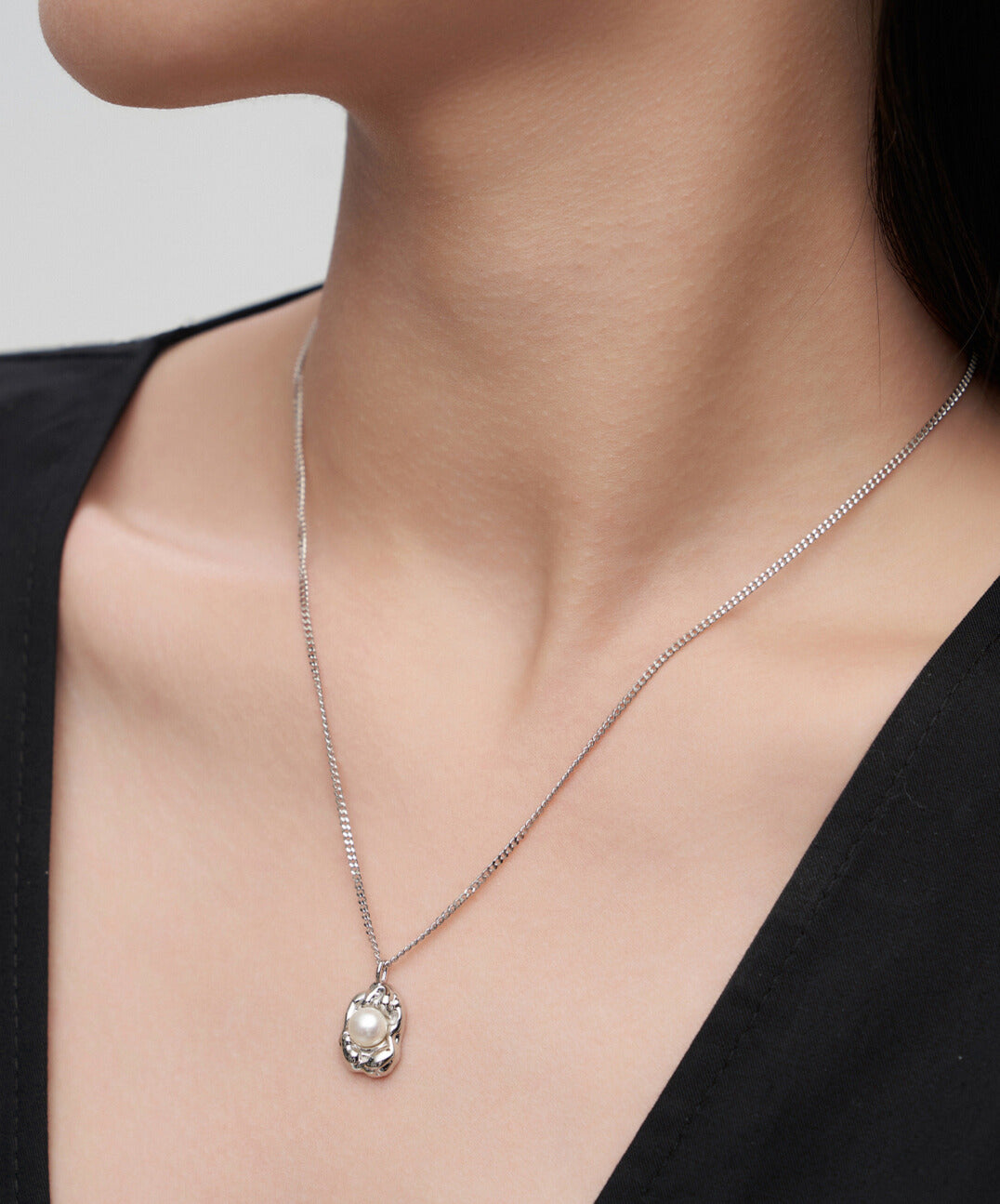 Model showcasing silver necklace featuring delicate flower charm and freshwater pearl.