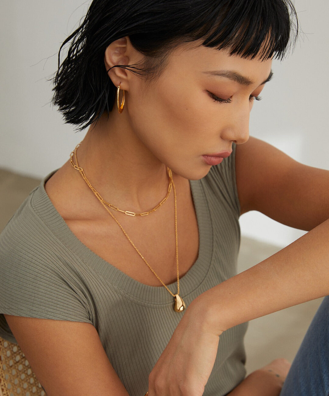 Female in green blouse adorned with gold necklaces.